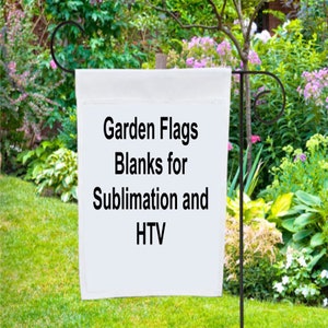 May include: A white garden flag blank, displayed outdoors on a black metal stand. The flag has the text "Garden Flags Blanks for Sublimation and HTV" in black. The background features lush green grass and a variety of plants and flowers.