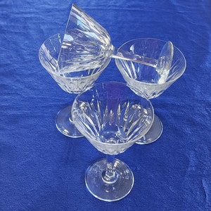 May include: Three clear glass stemmed wine glasses with a cut crystal design. The glasses are arranged in a triangular shape on a blue surface.