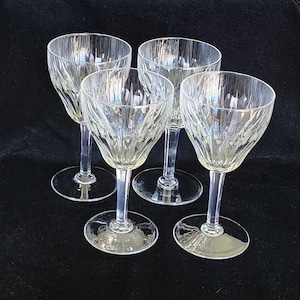 May include: Four clear glass wine glasses with a cut glass design. The glasses are arranged in a semi-circle on a black surface.