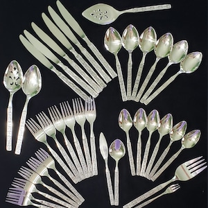 Könnte beinhalten: Ein Set aus silbernem Besteck mit einem verzierten Design. Das Set enthält Messer, Gabeln, Löffel und einen Servierlöffel.