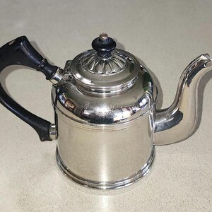 May include: A silver teapot with a black handle and a black knob on the lid. The teapot has a shiny, polished finish.