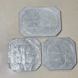 3 vintage Aluminum Hot Plate Holders with Dutch Holland Scenes. 2 are 6 X 6 inches and 1 is 6 X 8 inches.