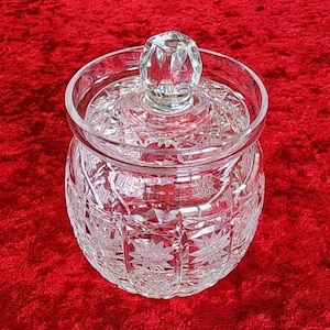May include: A clear glass jar with a lid, featuring a cut-glass design. The jar has a round body and a wide mouth. The lid has a knob on top.