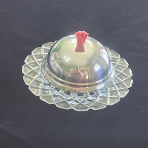 May include: A vintage silver butter dish with a glass base and a red plastic knob on the lid.