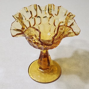 May include: A vintage amber glass candy dish with a ruffled edge and a pedestal base.