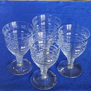 Peut inclure: Quatre verres à vin en verre transparent avec un motif en spirale. Les verres sont disposés en cercle sur une surface bleue.