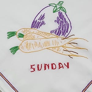 Puede incluir: Toalla de cocina bordada con una berenjena morada, tres zanahorias amarillas y la palabra "SUNDAY" en rojo.