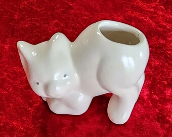 May include: White ceramic cat planter with a small opening on the top for planting. The cat is in a sitting position with its head tilted down.