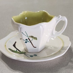 Könnte beinhalten: Ein weißes Tee-Set mit grünem Rand und grünem Blumendesign. Die Tasse hat einen gewellten Rand und einen Henkel.