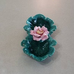 Op de afbeelding: Een groene keramische schaal in de vorm van twee koolbladeren met een roze bloem in het midden.