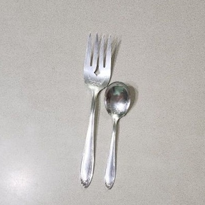Puede incluir: Un juego de tenedor y cuchara de plata. El tenedor tiene un diseño decorativo y la cuchara tiene un cuenco redondeado.
