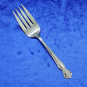 May include: A silver fork with an ornate handle. The fork has four tines and a decorative design on the handle.