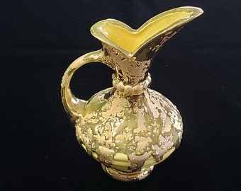 May include: A gold ceramic pitcher with a yellow glaze and a textured surface. The pitcher has a wide mouth and a handle.