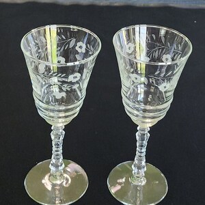 Puede incluir: Dos copas de vino de vidrio transparente con diseños florales grabados. Las copas tienen una base con tallo y un cuenco redondo.