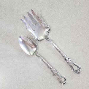 May include: A silver serving set with a fork and spoon. The fork has a decorative handle with a floral design. The spoon has a similar design on the handle.