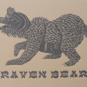 May include: A black and white illustration of a raven bear, a mythical creature with the head of a raven and the body of a bear. The image is on a light brown background with the text "RAVEN BEAR" printed below the creature.