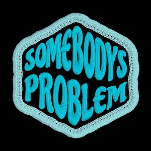 May include: A blue embroidered patch with the text "Somebody's Problem" in a white stitched outline.