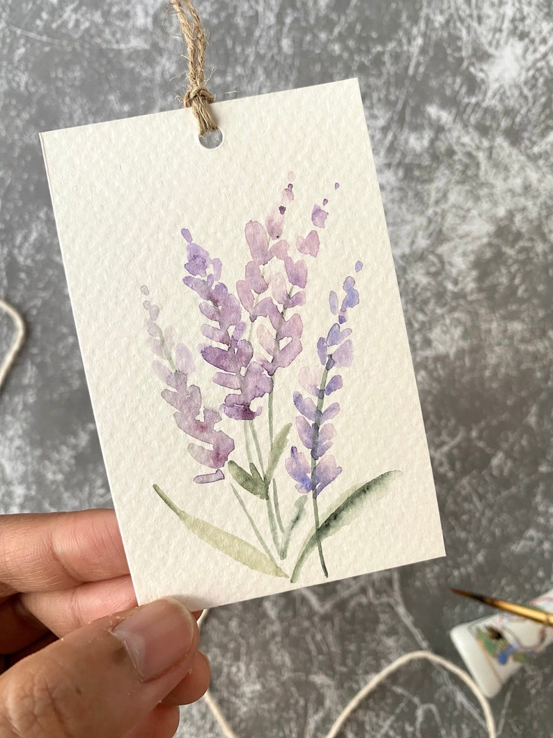 May include: A watercolor painting of lavender flowers on a white card with a hole punched in the top. The card is tied with twine.
