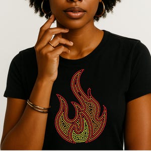 May include: Black t-shirt featuring a flame design made of red, orange, and yellow dots. The graphic is centered on the front of the shirt. The shirt has a crew neck and short sleeves.