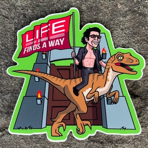 May include: A cartoon sticker featuring a man riding a velociraptor. The man is wearing a black shirt and jeans. The velociraptor is green and brown. The sticker has a green background and a red flag with the words "Life uh-huh finds a way" on it.