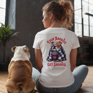 Könnte beinhalten: Weißes T-Shirt mit einem Bulldoggen-Motiv, das eine 3D-Brille trägt, Popcorn hält und in eine Decke gehüllt ist. Der Text auf dem Shirt lautet „Even Baddies Get Saddies“ und „And Need Movies and Snacks“. Ein Bulldogge ist ebenfalls im Bild.