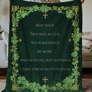 Puede incluir: Una manta verde oscuro con un borde dorado de nudos celtas y tréboles. La manta tiene el texto "May your troubles be less, your blessings be more, and nothing but happiness come through your door."