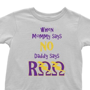 Könnte beinhalten: Ein hellgraues T-Shirt mit dem Text "When Mommy Says No Daddy Says R22" in lila und goldenen Glitzerbuchstaben.