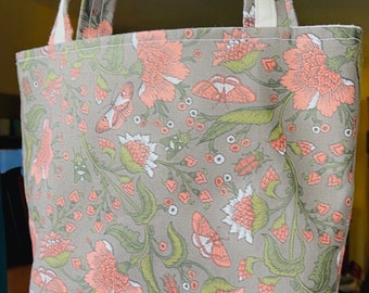 May include: A gray and coral tote bag with a floral print featuring butterflies and flowers. The bag has two long straps.