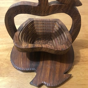 May include: A wooden apple-shaped fruit bowl with a carved design. The bowl is made of dark brown wood and has a handle.