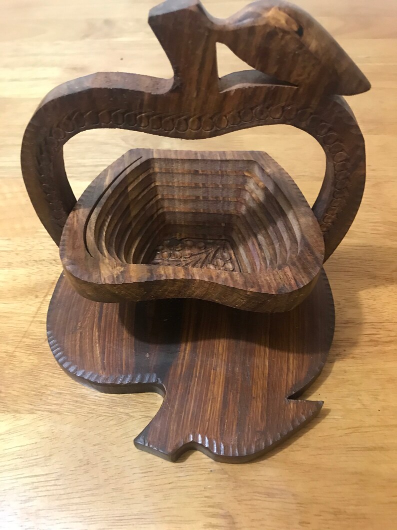 May include: A wooden apple-shaped fruit bowl with a carved design. The bowl is made of dark brown wood and has a handle.