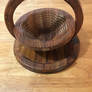 Puede incluir: Un frutero de madera con un asa tallada. El cuenco est&aacute; hecho de m&uacute;ltiples capas de madera y tiene un dise&ntilde;o decorativo. El cuenco es de color marr&oacute;n y tiene un acabado natural.
