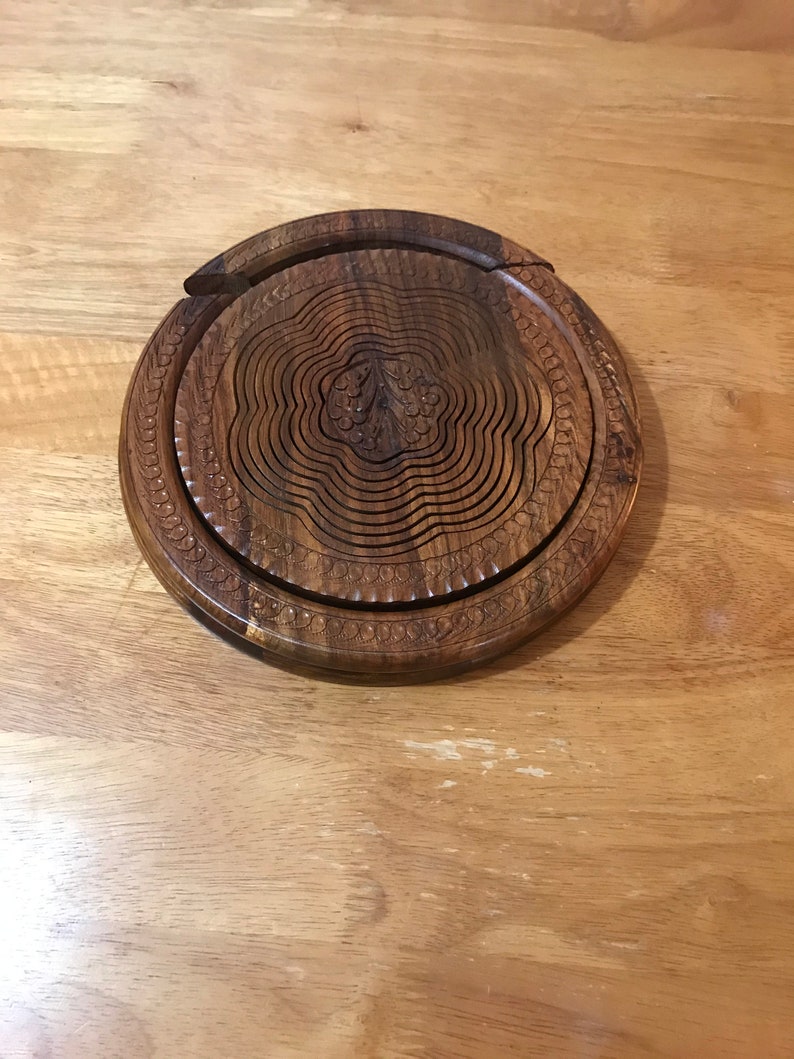 Puede incluir: Un bol de fruta redondo de madera extensible con un dise&ntilde;o floral tallado. El bol est&aacute; hecho de madera marr&oacute;n oscura y tiene un acabado natural.