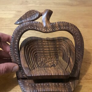May include: A wooden apple-shaped fruit bowl with intricate carvings. The bowl is made of dark brown wood and has a leaf design on the top. The bowl is collapsible and can be folded flat for storage.
