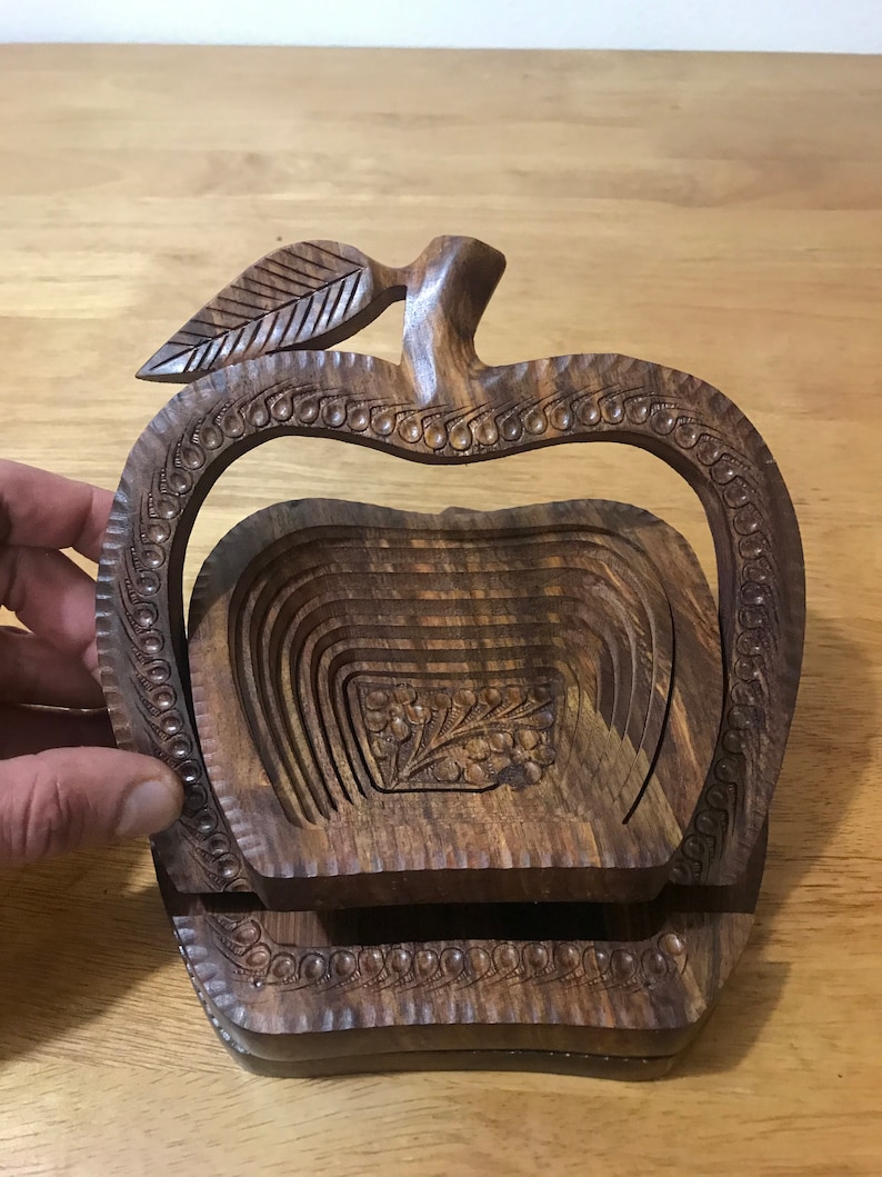 May include: A wooden apple-shaped fruit bowl with intricate carvings. The bowl is made of dark brown wood and has a leaf design on the top. The bowl is collapsible and can be folded flat for storage.