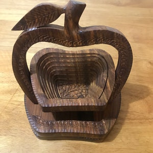 May include: A wooden apple-shaped fruit bowl with a carved leaf on top. The bowl is made of dark brown wood and has a layered design.