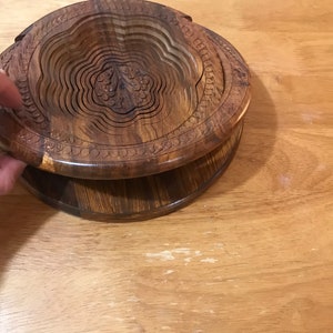 Puede incluir: Un cuenco de madera con un dise&ntilde;o floral tallado. El cuenco est&aacute; hecho de m&uacute;ltiples capas de madera que se pueden plegar para su almacenamiento.