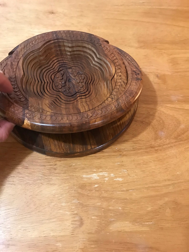 Puede incluir: Un cuenco de madera con un dise&ntilde;o floral tallado. El cuenco est&aacute; hecho de m&uacute;ltiples capas de madera que se pueden plegar para su almacenamiento.