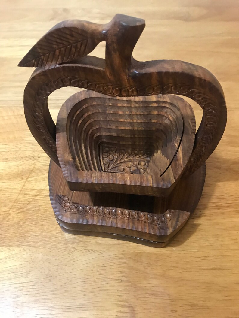 May include: A wooden apple-shaped fruit bowl with a carved leaf on top. The bowl is made of dark brown wood and has a layered design.