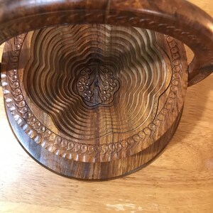 Puede incluir: Un frutero de madera con un dise&ntilde;o tallado y un asa. El frutero es de madera oscura y tiene forma circular.