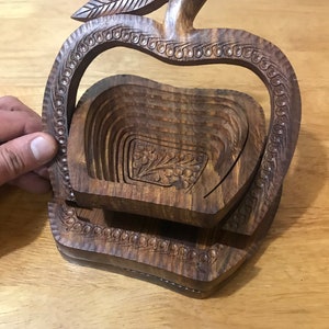 May include: A wooden apple-shaped fruit bowl with a carved leaf design. The bowl is made of multiple layers of wood that can be folded to create a compact storage solution.