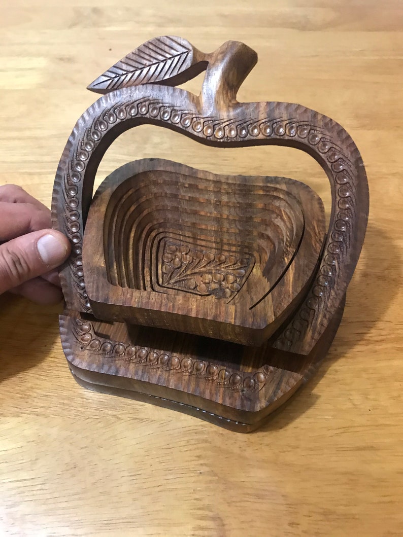 May include: A wooden apple-shaped fruit bowl with a carved leaf design. The bowl is made of multiple layers of wood that can be folded to create a compact storage solution.