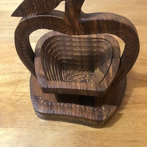 May include: A wooden apple-shaped fruit bowl with a carved leaf on top. The bowl is made of dark brown wood and has a layered design.