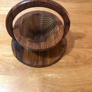 Puede incluir: Un frutero de madera con un dise&ntilde;o tallado y un asa. El frutero est&aacute; hecho de madera oscura y tiene un dise&ntilde;o en capas.