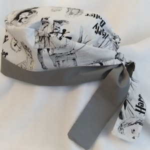 May include: A gray and white patterned surgical scrub hat with a gray tie. The pattern features a black and white illustration of a wizard with the text "Harry Potter" on the hat.