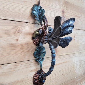 Può includere: Un battente per porta decorativo a forma di libellula in metallo. Le ali sono grigio scuro e il corpo è blu strutturato. Le foglie sono verde acqua e la base è color rame. Il battente è montato su una porta di legno.