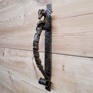 May include: A black metal door handle with a ram's head design. The handle is ornate and has a textured finish.