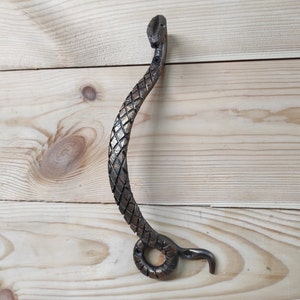 Puede incluir: Una manija de puerta decorativa con forma de serpiente con un diseño texturizado y escamoso. La manija es de metal y tiene un acabado bronce.