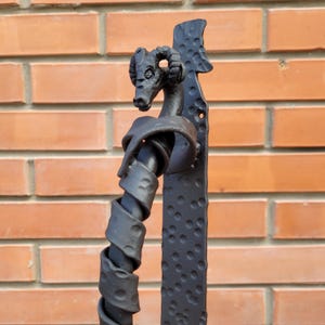 Puede incluir: Pomo de puerta de metal negro con un diseño de cabeza de carnero. El pomo está retorcido y tiene un acabado texturizado.