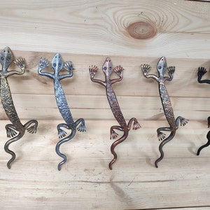 May include: Five metal lizard door handles in different finishes: gold, silver, copper, black, and bronze. The handles are all in the same design, with a lizard shape and a textured surface.