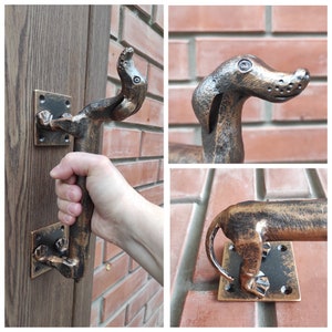 May include: A bronze dachshund-shaped door handle with a textured finish. The handle is mounted on a wooden door and a brick wall.